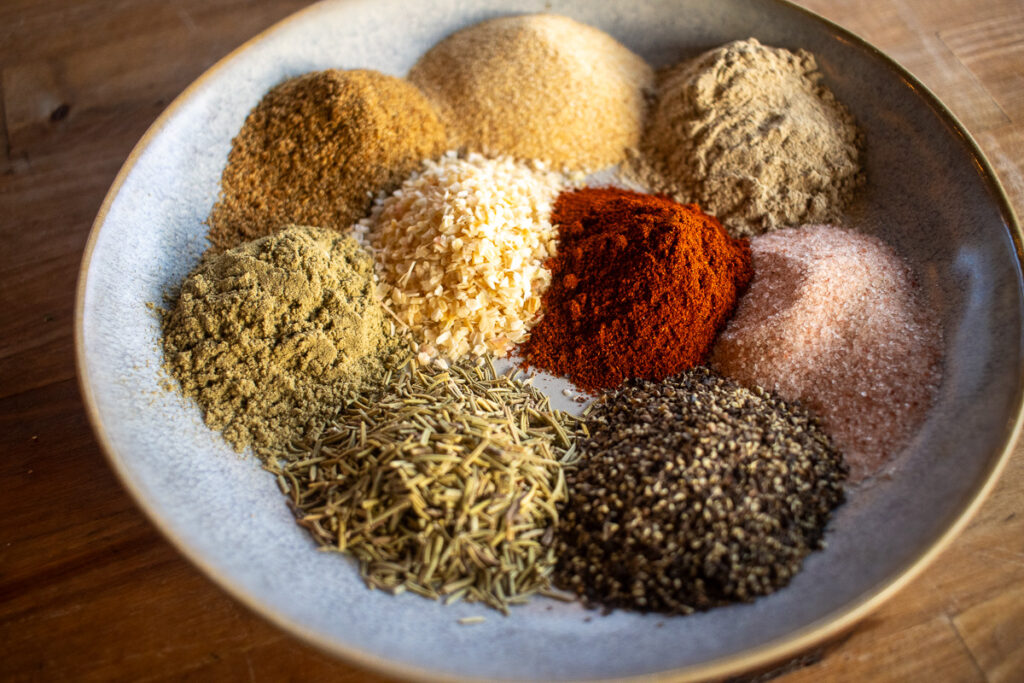 A bowl showcasing a vibrant homemade turkey seasoning blend, featuring a variety of spices like smoked paprika, ground pepper, garlic granules, rosemary, and pink salt, perfectly arranged for a flavorful turkey rub.