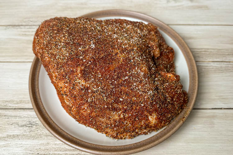 raw turkey breast coated in rub on a white plate