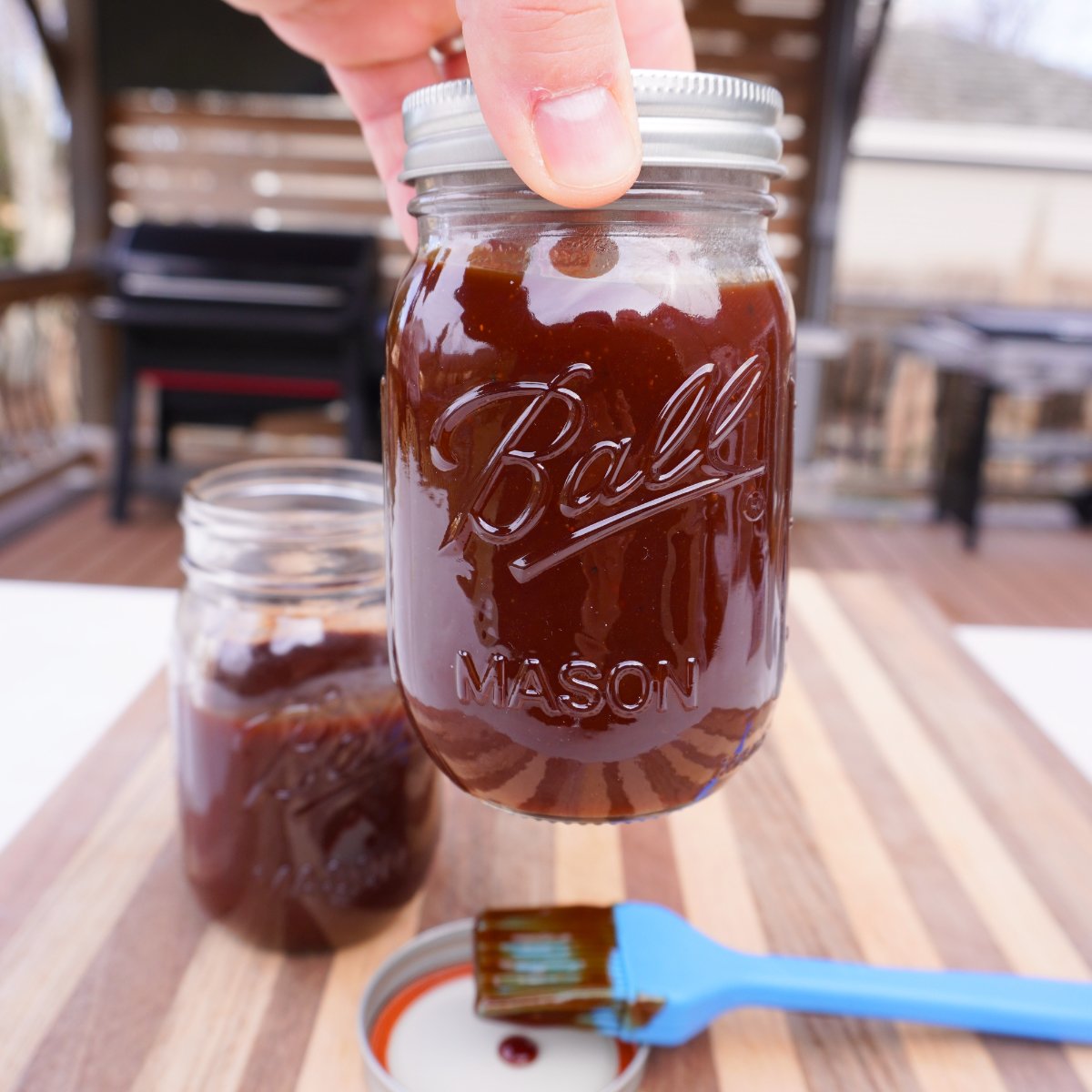 sweet and tangy bbq sauce in a mason jar listed to show off.  Behind left over sauce and a dirty brush.