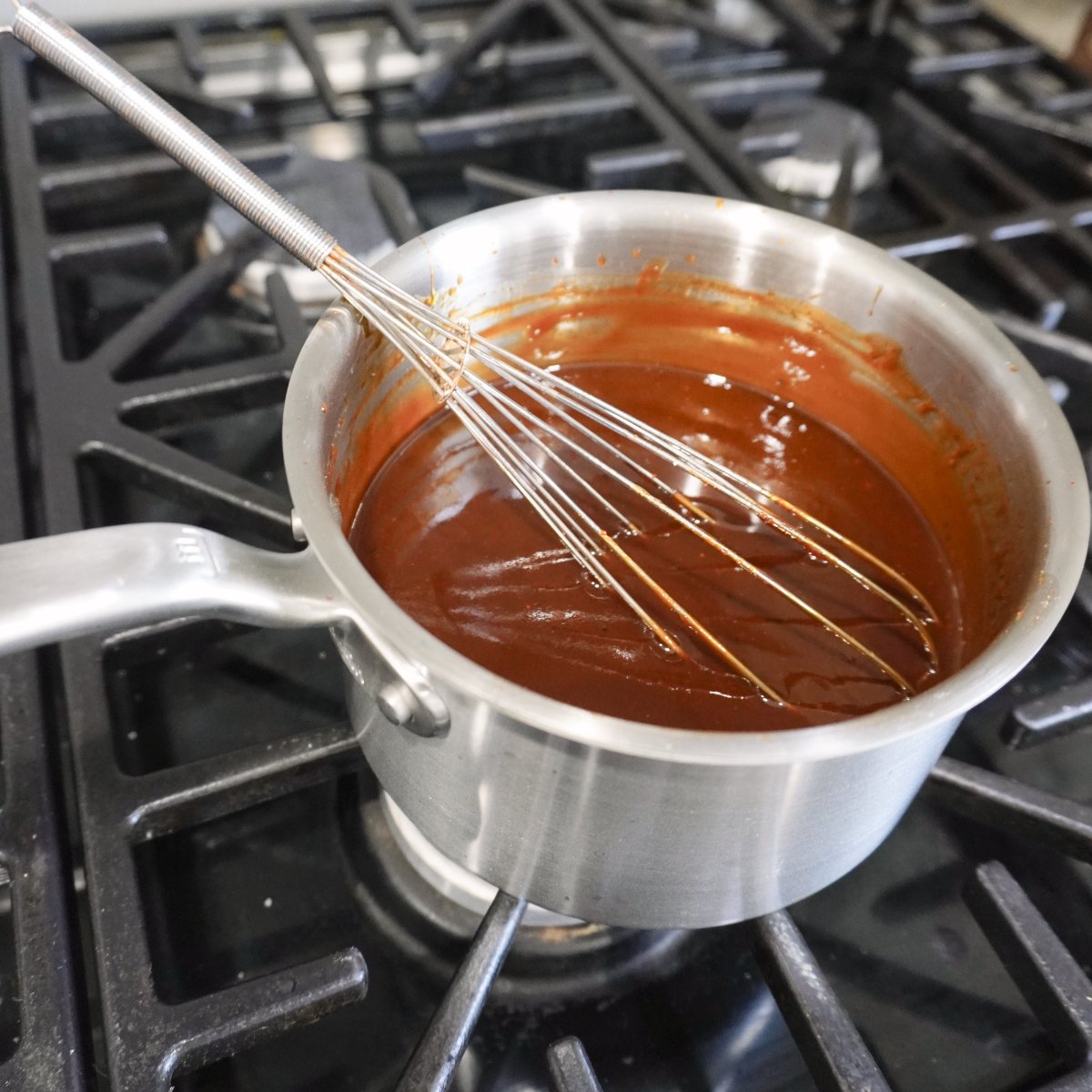 BBQ sauce in a sauce pan on the stove with a whisk inside.