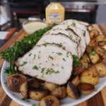 Grilled mustard pork loin sliced on a plate with roasted potatoes and brocolini.