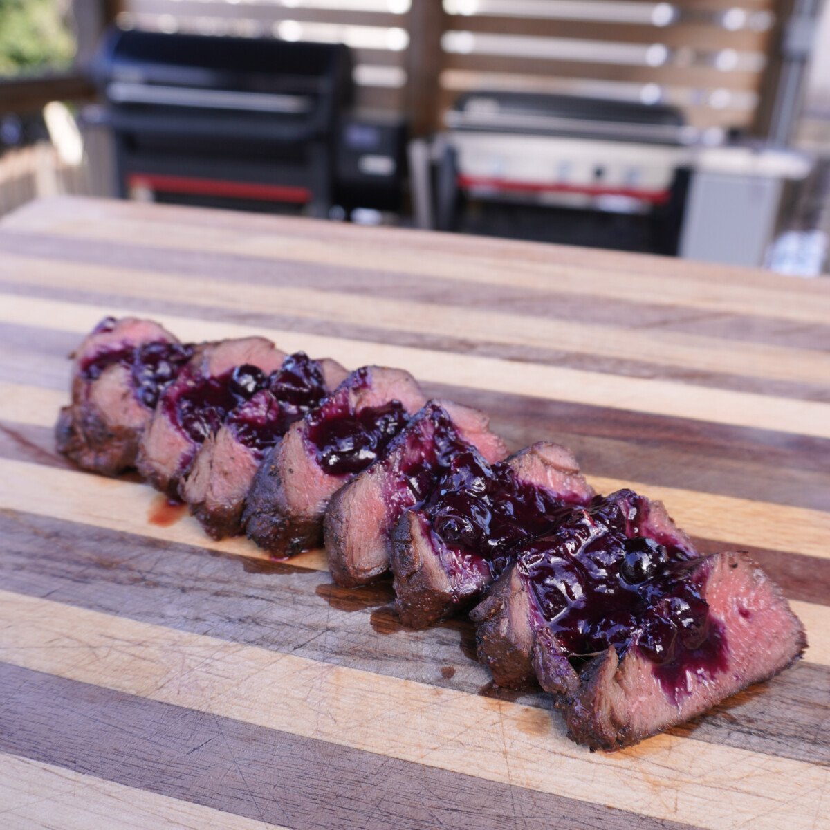 Perfectly grilled venison tenderloin sliced on a cutting board topped with blueberry sauce.