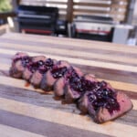 Perfectly grilled venison tenderloin sliced on a cutting board topped with blueberry sauce.