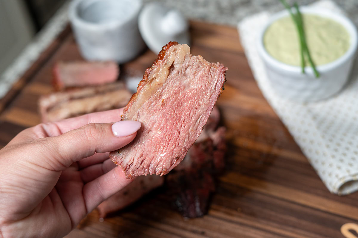 a lovely manicured hand holding a slice of cooked tri-tip steak