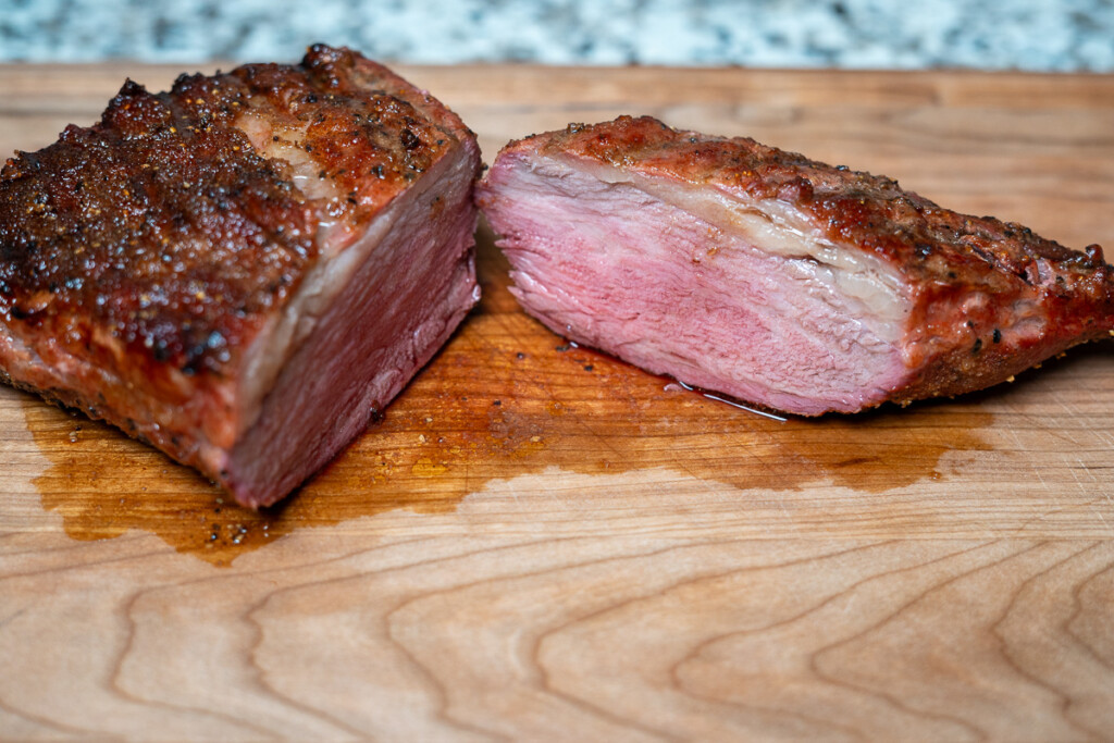 a whole cooked tri-tip cut in half on a wooden board