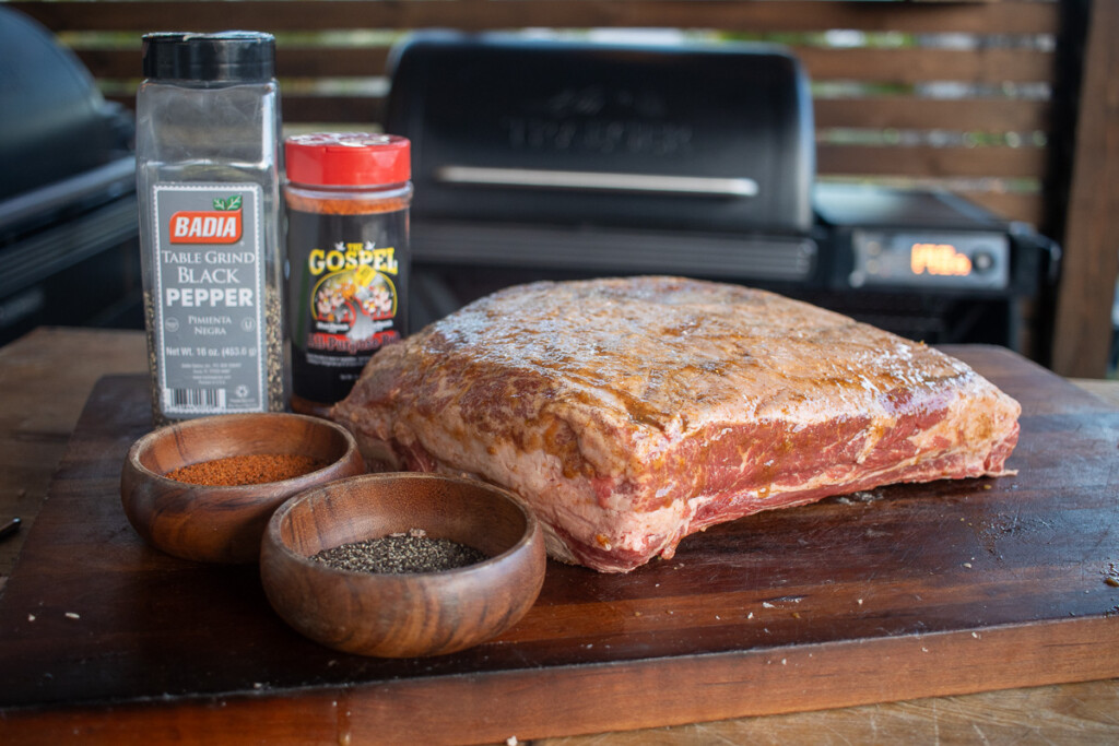 a raw beef rib with jars of seasong and a bowl of cracked black pepper