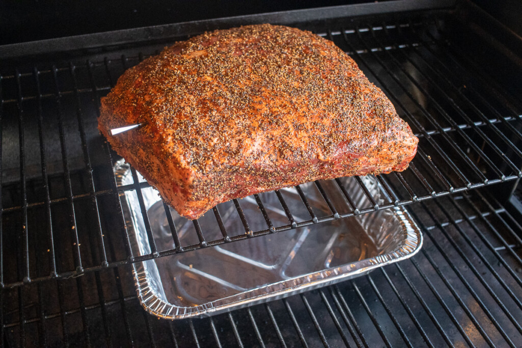 a raw prime rib in the smoker with a thermometer in it and a foil tray underneath