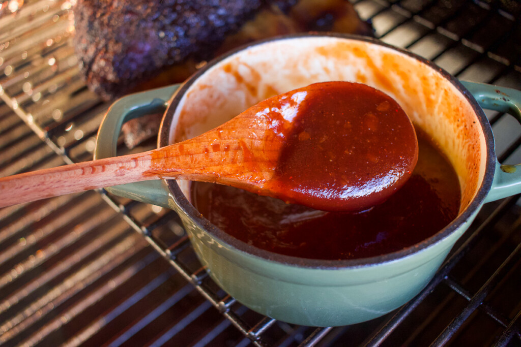 a pot of bourbon sauce with a wooden spoonful of sauce