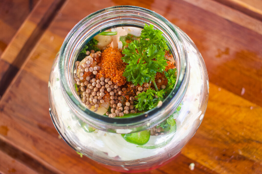 a glass jar with onions, jalapeno, coriander and spices in it