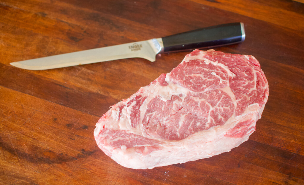 a raw ribeye steak and a knife on a wooden chopping board