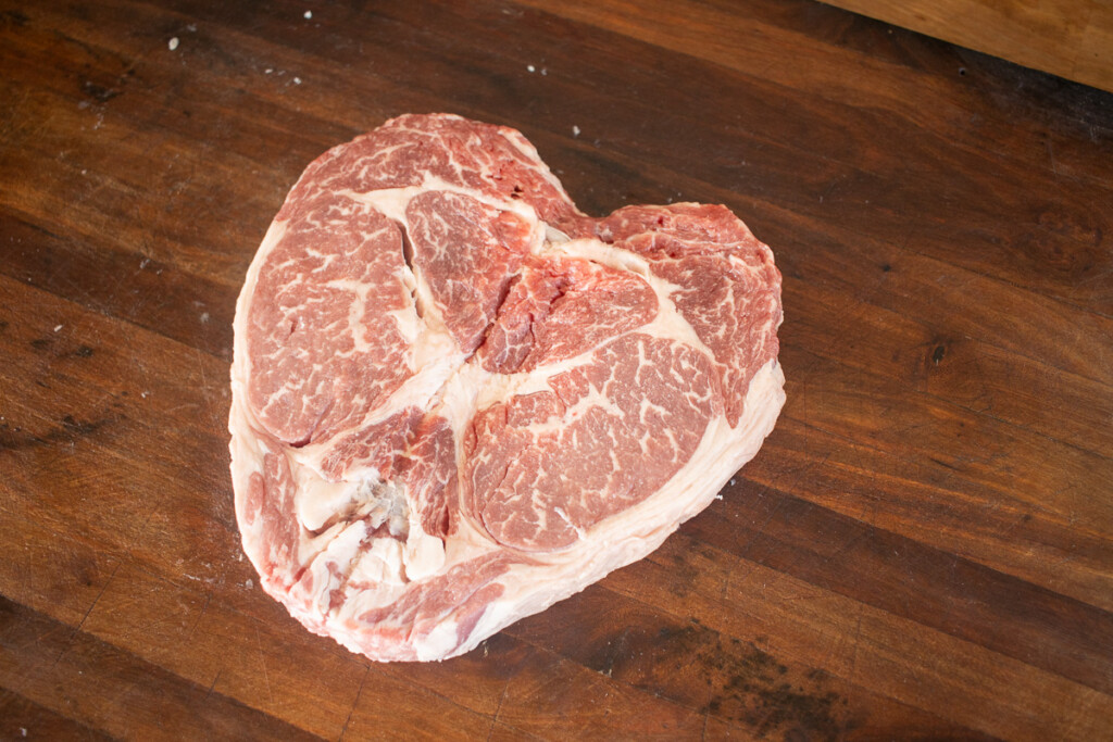 a raw heart-shaped ribeye steak on a wooden board