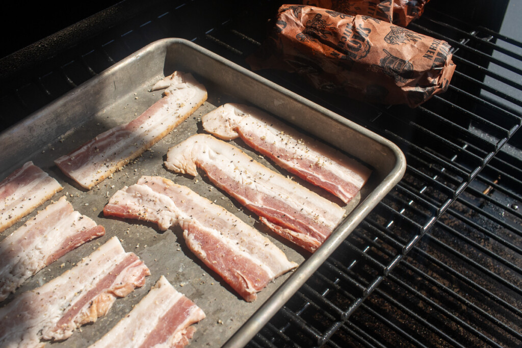 rashers of raw bacon on a baking sheet in the smoker