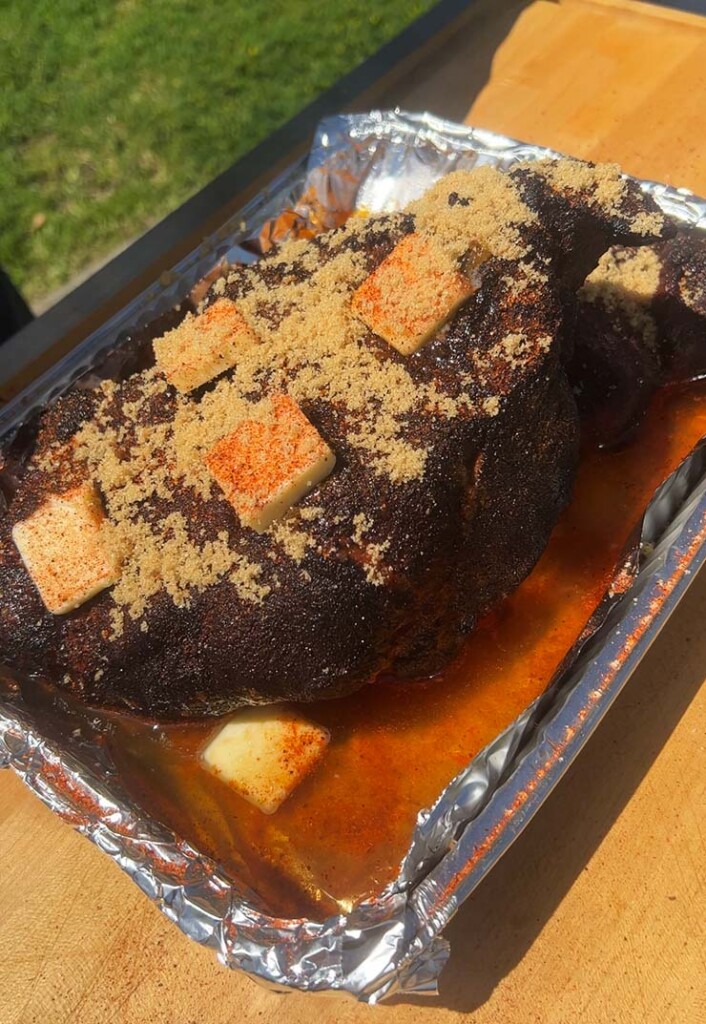 pork butt covered in butter and brown sugar in an aluminum foil tray