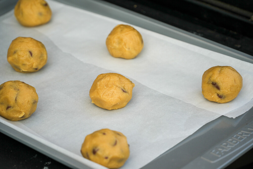 three balls of uncooked cookie dough on a baking paper line tray