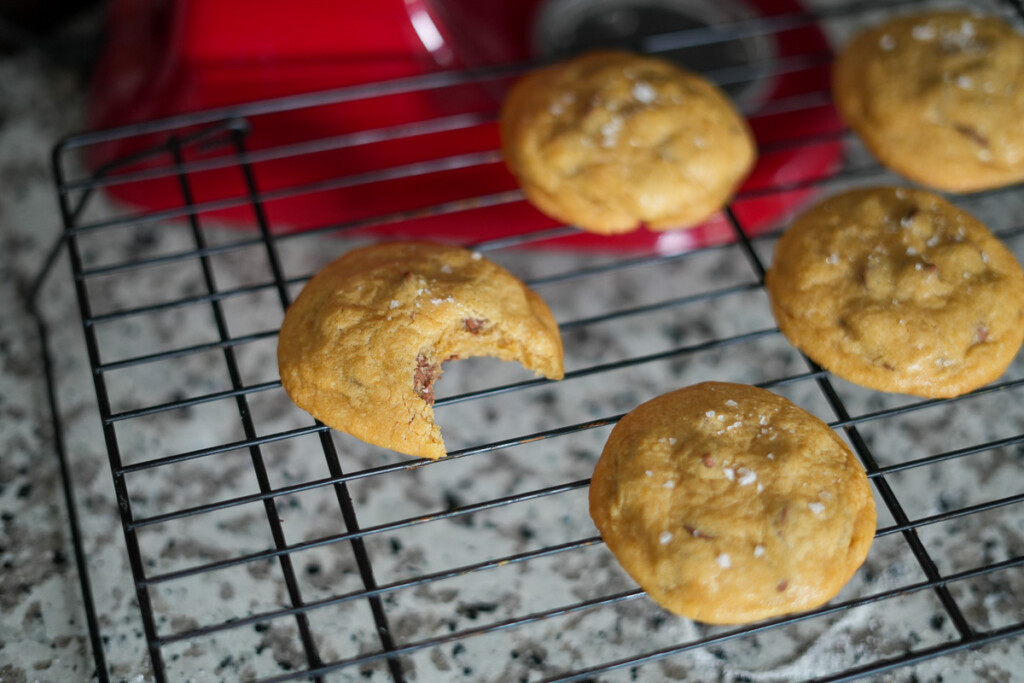 chocolate chip cookies cooling on a wire rack, one of them has a bite taken out of it