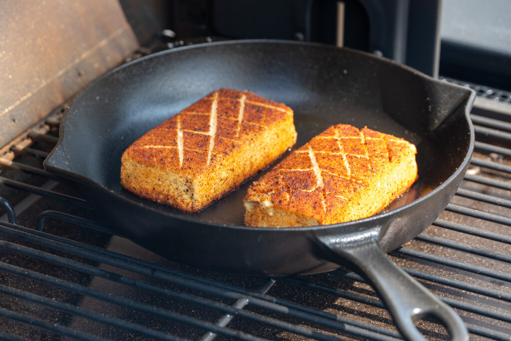 Smoked cream cheese in a cast iron skillet, starting to soften and develop a deep golden crust.