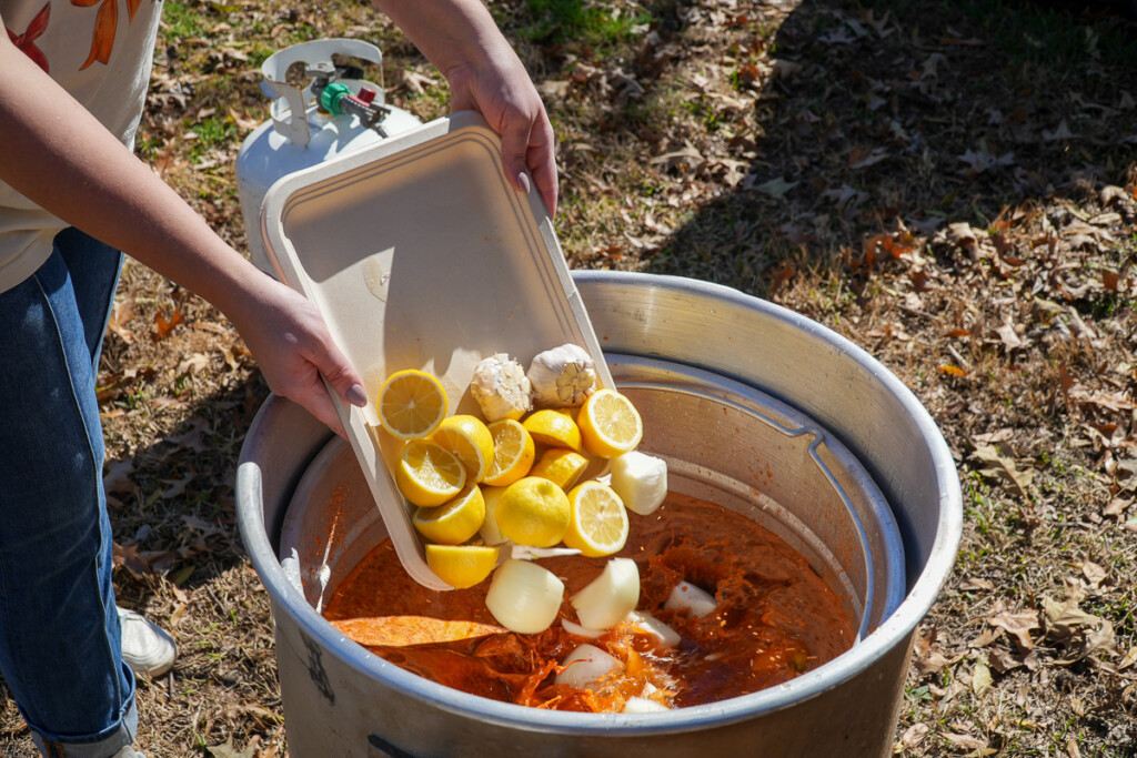 lemons, garlic and onions being tipped into a stockpot of seasoned water