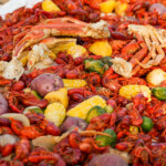 A traditional Louisiana crawfish boil spread across a table, featuring bright red crawfish, corn on the cob, red potatoes, Brussels sprouts, lemons, and crab legs, all seasoned with bold Cajun spices. A bowl of dipping sauce sits on the side, ready for serving.