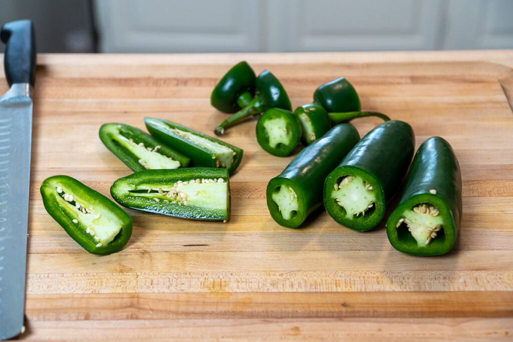 jalapenos on a wooden chopping board with the tops cut off and some cut in half