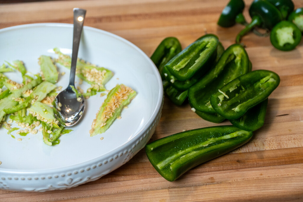 halved jalapens with seeds removed with a white plate with discarded seeds