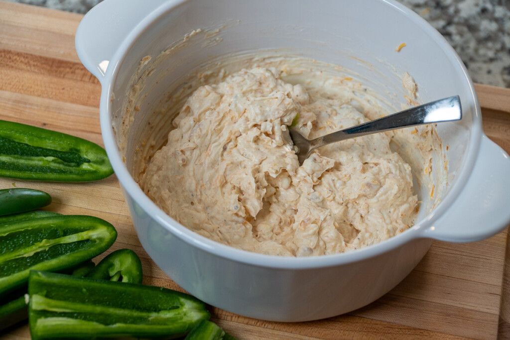 a bowl of smoked cream cheese and shredded cheddar mixed  together in a white bowl with a spoon