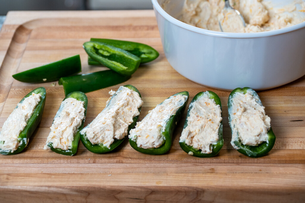 uncooked stuffed jalapeno halves on a wooden board