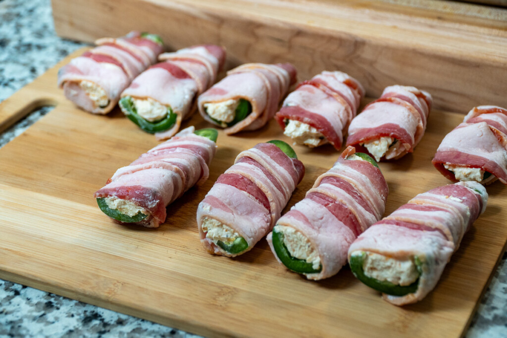 raw bacon wrapped jalapeno poppers on a wooden board