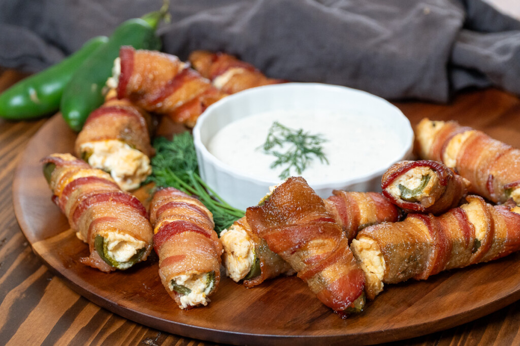 a bowl of ranch dipping sauce surrounded jalapeno poppers