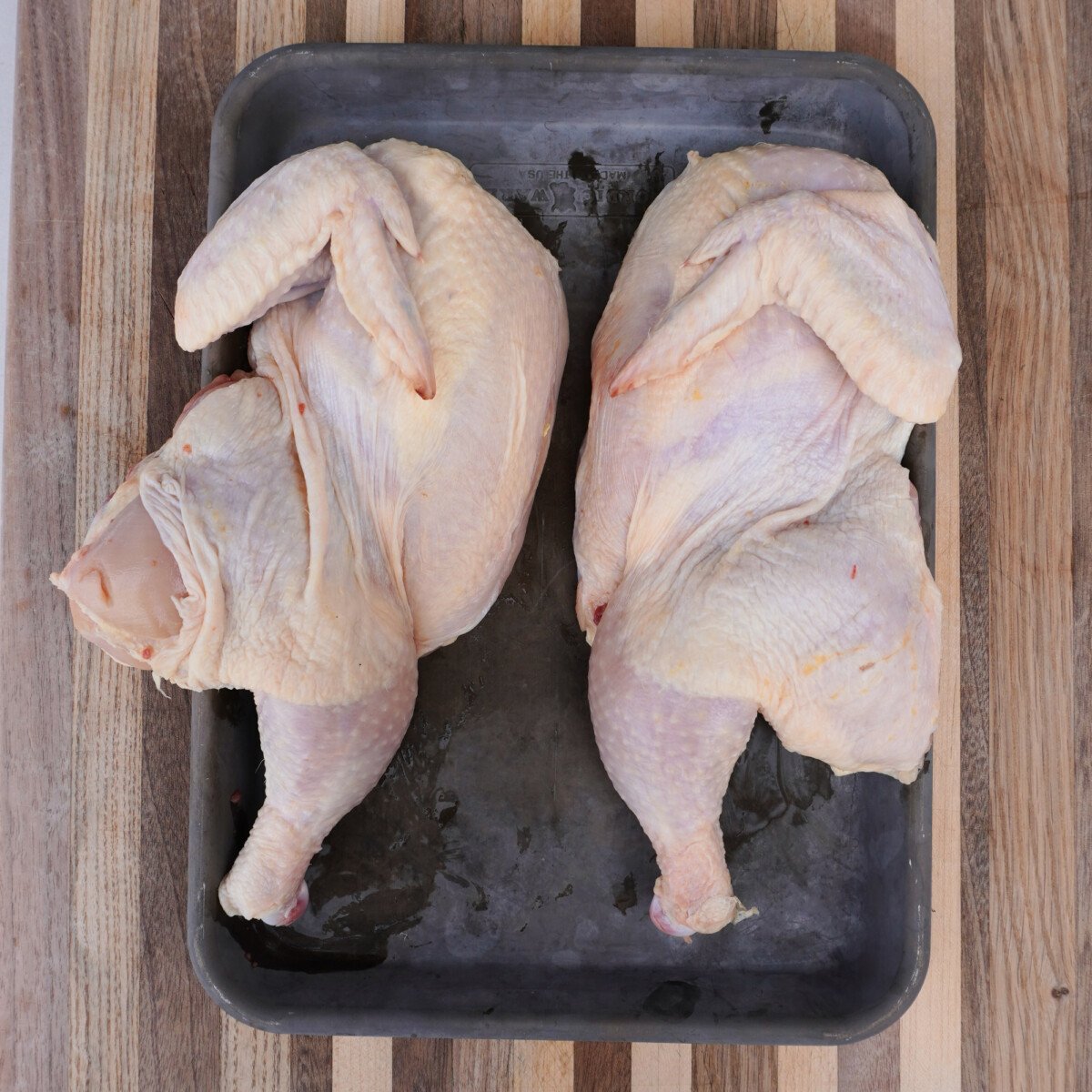 raw chicken halves on a tray.