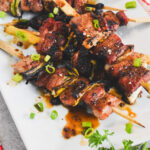 A platter of grilled pork belly skewers topped with scallions.