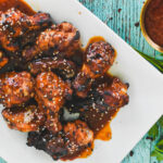 A white platter of gochujang chicken wings topped with white sesame seeds.