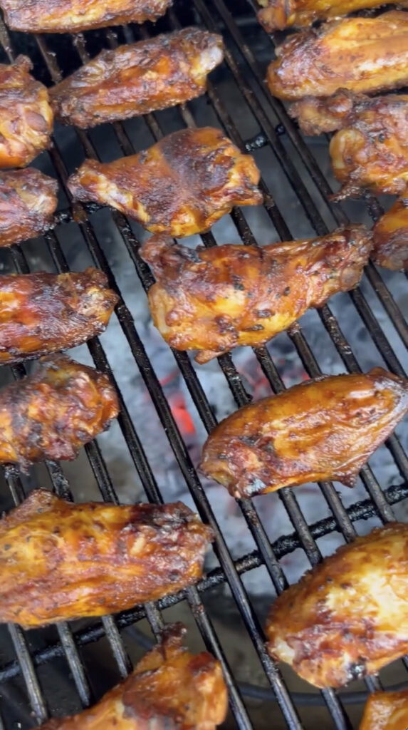 Close-up of smoked lemon pepper chicken wings on a grill, crisping up over hot coals for a final sear.