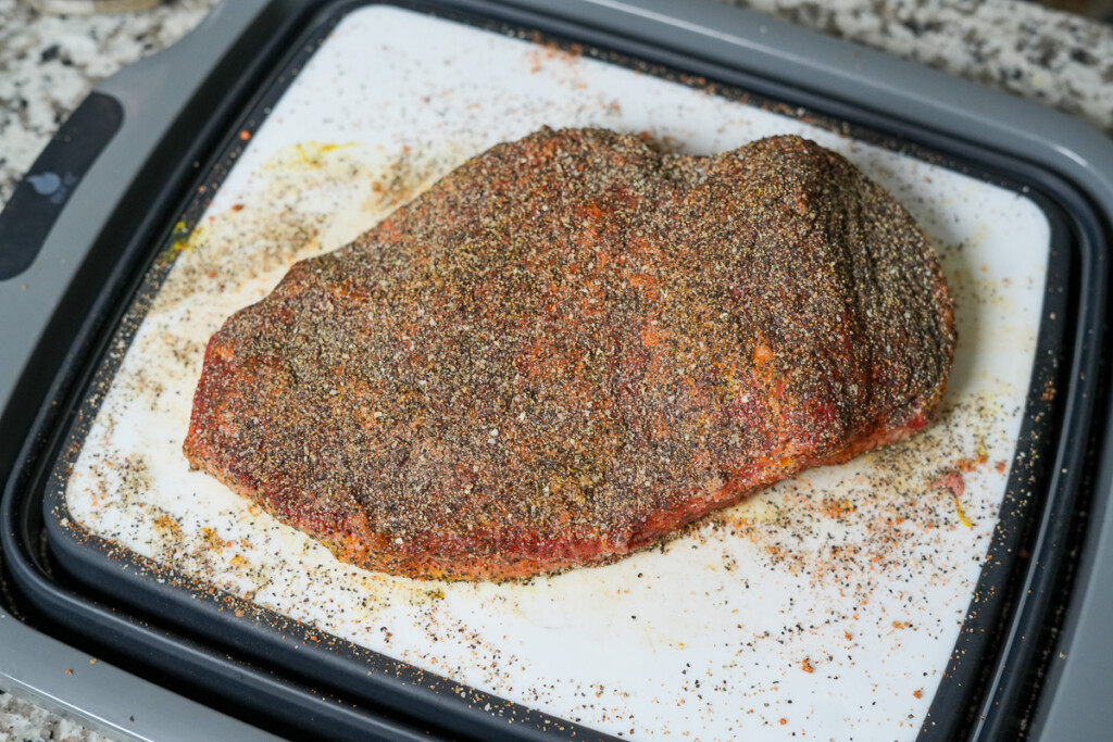 a raw seasoned brisket flat on a white board