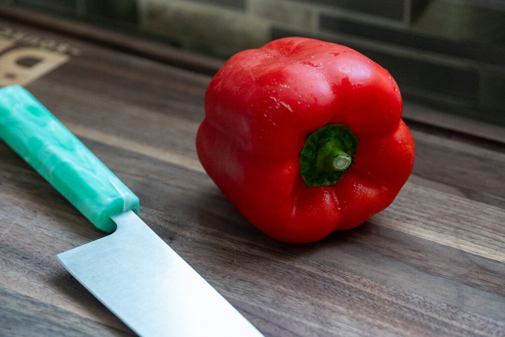 a red bell pepper and a knife with a green handle on a wooden chopping board