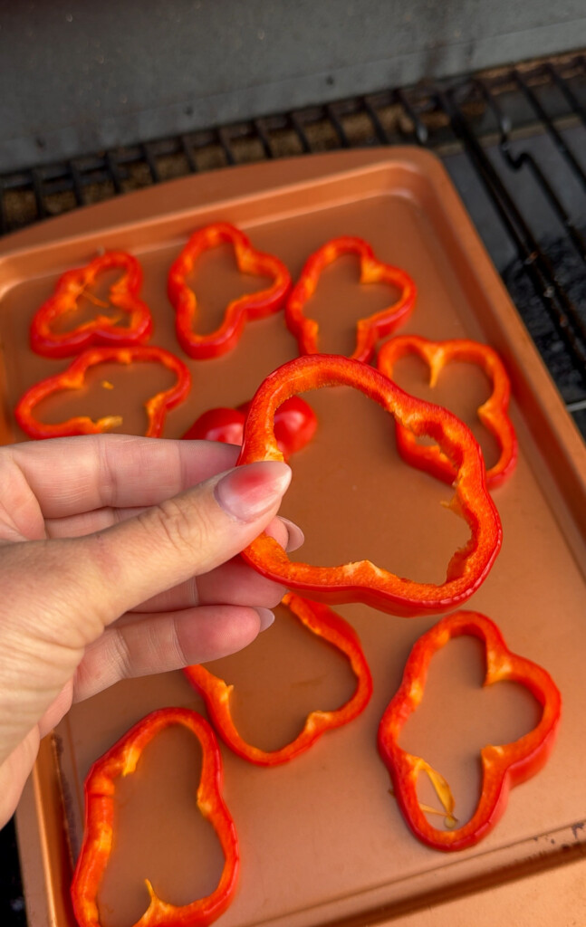 a hand holding a slice of red bell pepper and a tray of bell pepper slice in the background