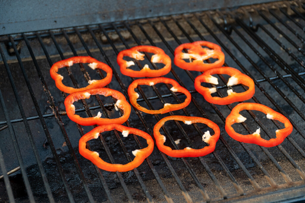 sliced of red bell pepper on the grill grates in the smoker