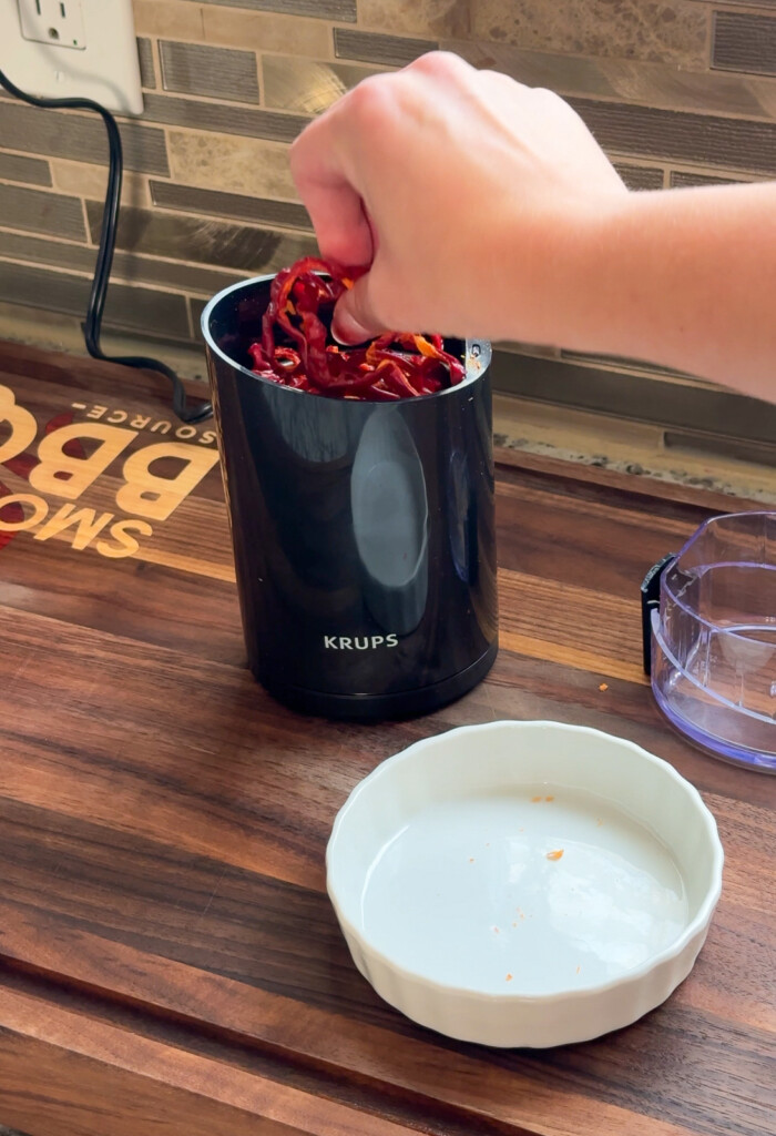 a hand putting dehydrated bell peppers into a  grinder