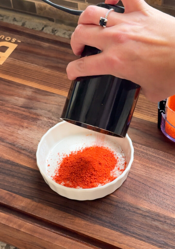 ground bell pepper being tipped from the grinder into a white bowl.