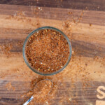 Homemade pork dry rub seasoning in a glass jar on a wooden board with spoonful of spice blend – perfect BBQ rub for ribs, pulled pork, or chops