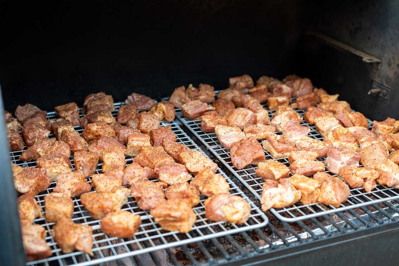 Seasoned pork belly cubes arranged on wire racks inside a smoker, beginning the first phase of cooking to develop bark for burnt ends.