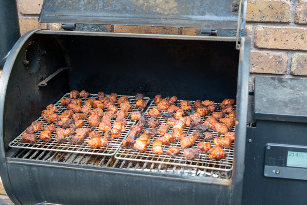 Smoked pork belly burnt ends on wire racks inside a smoker, showing well-developed bark after several hours of cooking.