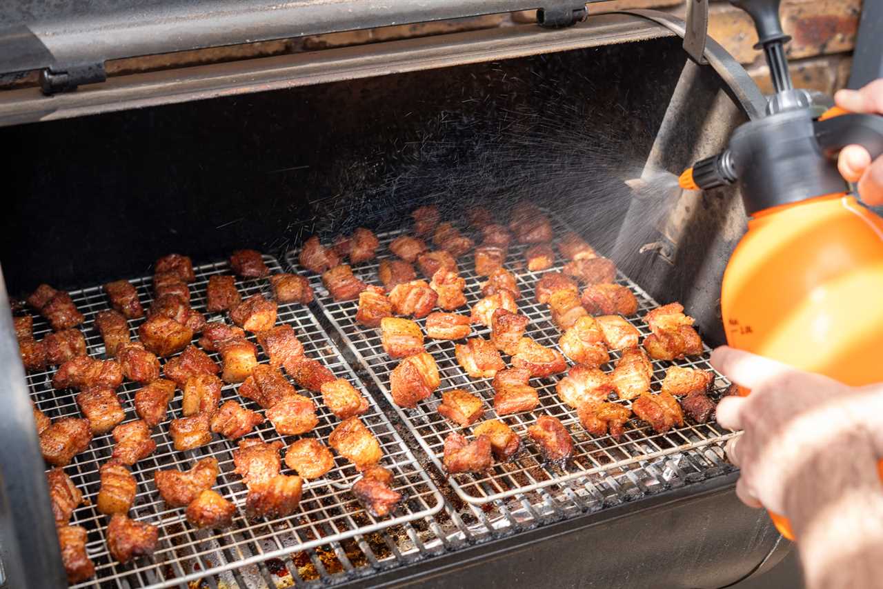 Pork belly burnt ends being spritzed with liquid inside a smoker, helping to keep them moist and develop bark during the smoking process.