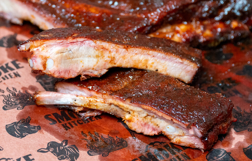 Close-up of 3-2-1 smoked pork ribs on a cutting board, featuring a sticky glaze and smoke ring, with juicy meat pulling away from the bone.