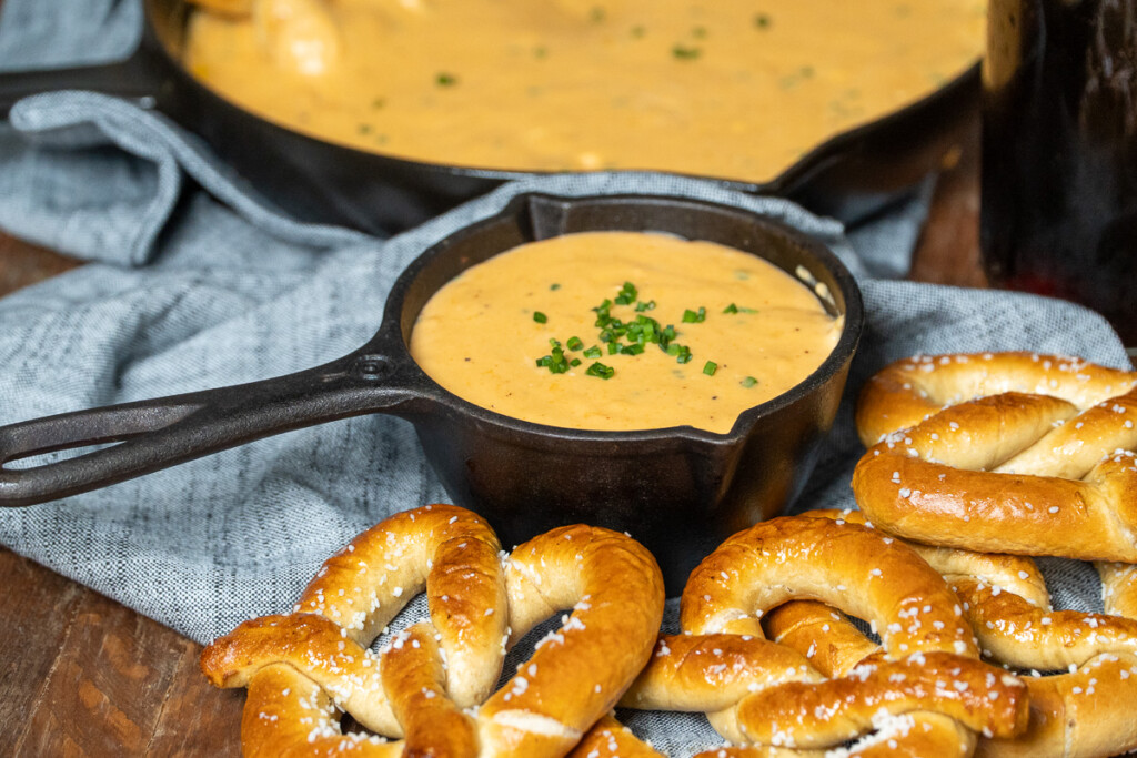 a skillet of smoked beer cheese dip with pretzels in the forground