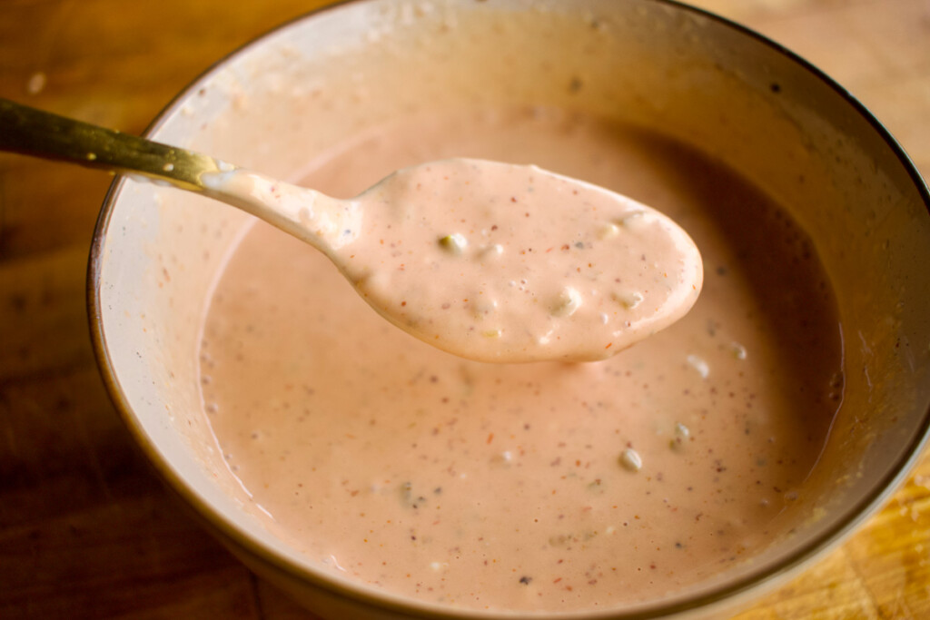 a bowl of orange burger sauce with a spoon scooping some out