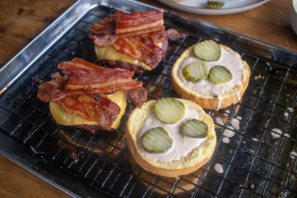 burger assembly. one half patty, cheese and bacon, the other half sauce and pickles