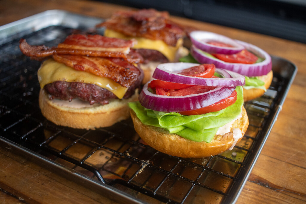 burger assembly. one half patty, cheese, bacon. the other half sauce, pickles, lettuce, tomato, onion