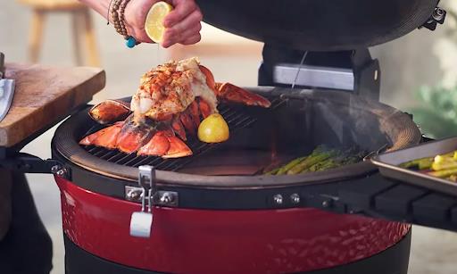 A woman squeezing a lemon over a lobster on a red grill.