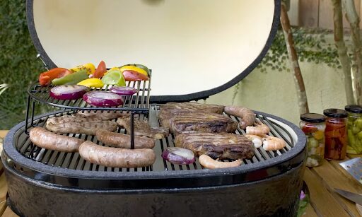 An oval shaped grill with meats and veggies on it.