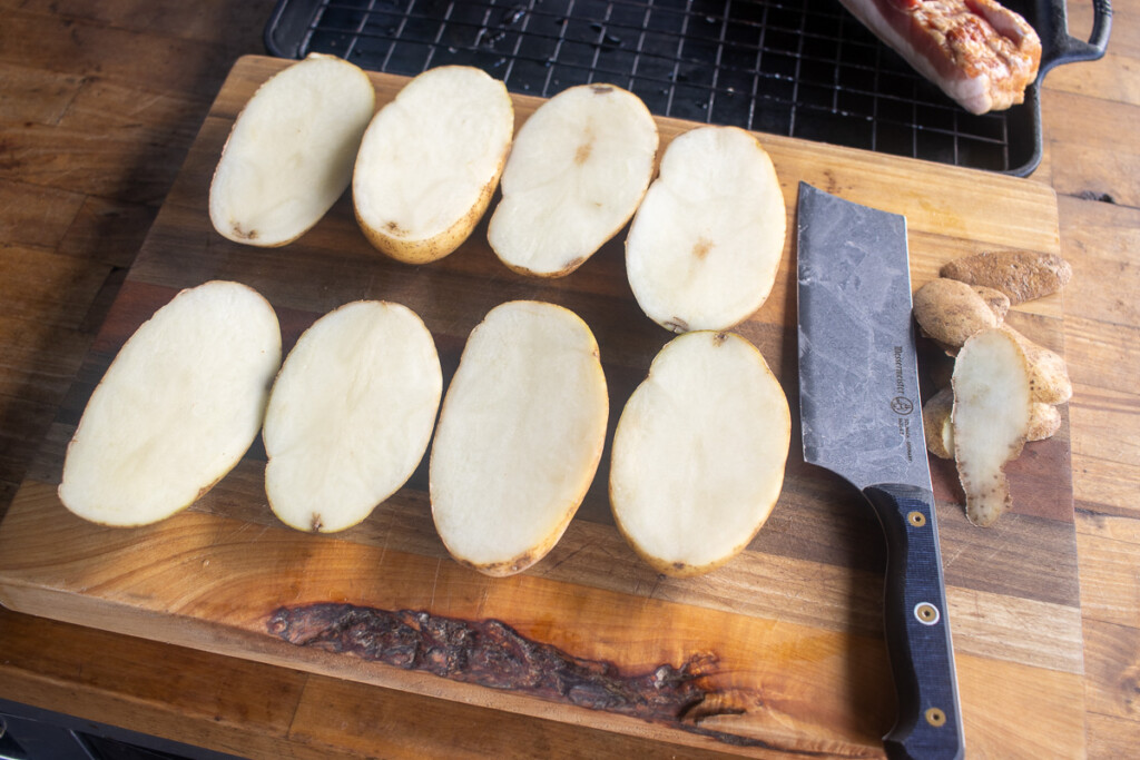 raw potatoes cut in half on a wooden board with a knife next to them